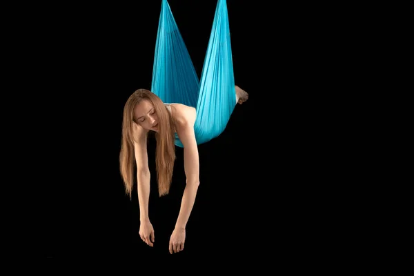 Tired young woman during gymnastic training session on sports hammock. Class of fly yoga. Black background.