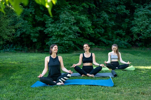 Morning yoga practice. Harmony and balance. Three young women in the park meditate sitting on yoga mats.