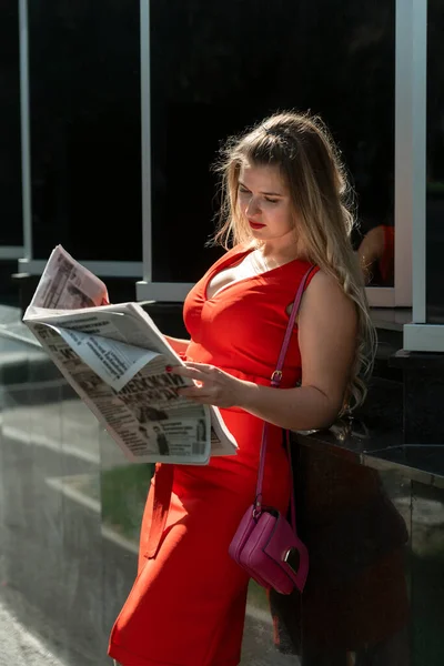 手に新聞を持つ成功した女性の肖像 赤いドレスの美しい実業家は新聞を読む — ストック写真