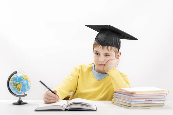 Gelangweilte Grundschüler Machen Hausaufgaben Hause Junge Studentenhut Schreibt Notizbuch Kind — Stockfoto