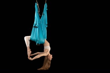 Beyaz spor giysili genç bir kadın siyah arka planda izole edilmiş hamak ile havadan ters çevirme anti-yerçekimi yogası yapıyor. Yan görünüm