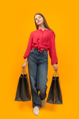 Stylish young girl holds several paper bags after shopping on yellow background. Black Friday Concept. Vertical frame
