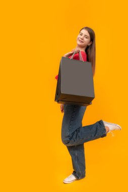 Sarı arka planda alışveriş yaptıktan sonra çantalı genç bir kız. Uzayı kopyala Model yap. Kara Cuma alışverişi
