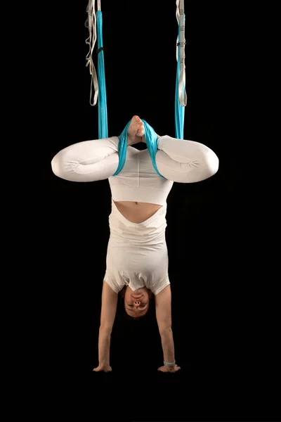 Girl practices fly yoga. Young woman upside down during an aerial gymnastics exercise. Isolated on black background