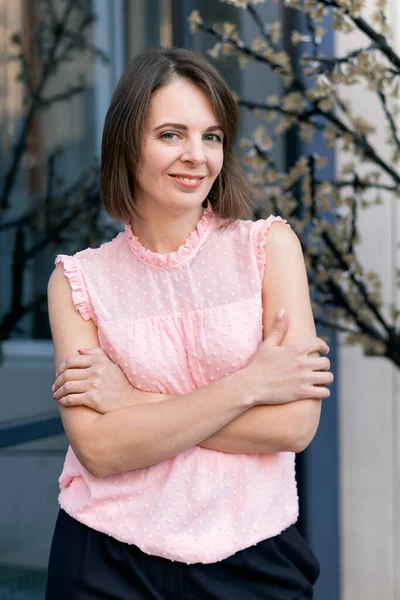 Smiling woman in pink blouse with bob haircut outside. Portrait of middle-aged woman