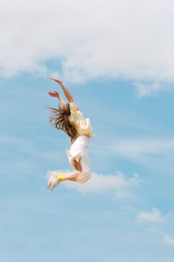 Yound woman flies in the sky raising her hands. Girl jumping through the air. Concept of freedom and happiness.