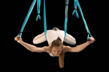 Woman practicing fly yoga using hammock suspended from the ceiling. Girl gymnast in trapeze class. Black background
