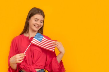 Studio portrait of young girl with USA flag on yellow background. Immigration to the United States. Student Exchange Program in America