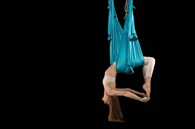 Young woman in hammock for doing pose of antigravity yoga. Sport girl performing air gymnastics exercise. Black background.