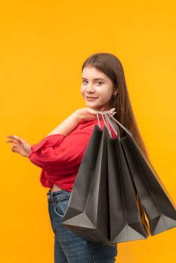 Young woman with big black shopping bags. Woman smiles after good shopping. Bright yellow background. Vertical frame