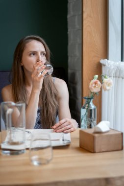 Woman with glass of water in her hands. Girl drinks water and looked in window.. Benefits of water. Vertical frame