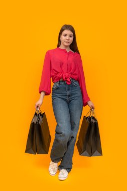 Portrait of young girl with paper bags in her hands on bright yellow background. Shopping concept. Vertical frame