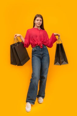 Attractive young girl with paper bags in her hands on bright yellow background. After shopping concept. Vertical frame