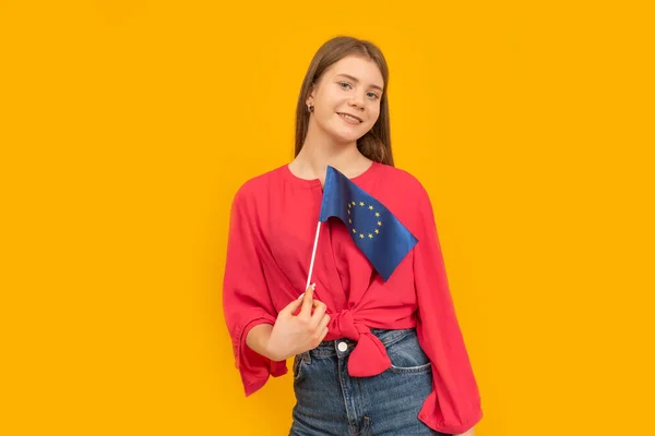 Portrait of smiling young girl with the EU flag in her hands. Yellow background. Study in Europe. Space for text.