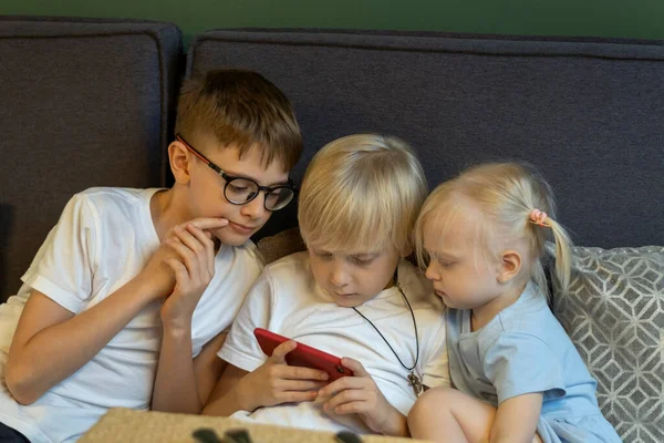 Three Children Sit Couch Look Phone Siblings Enthusiastically Look Screen — ストック写真