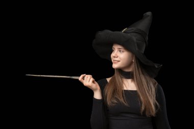 Young witch in pointed hat with magic wand in hands. Copy space for text. Isolated on black background. Halloween costume clipart
