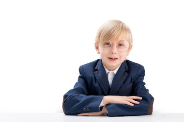 Elementary school student wears glasses sit idly by at desk. Portrait of blond schoolboy on white background. Fidget boy