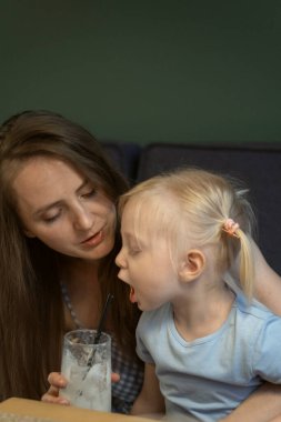 Mother and little daughter in cafe. Child opened his mouth to reach for straw for cocktail. Vertical frame