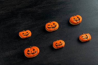 Balkabağı şeklinde turuncu zencefilli ekmek Cadılar Bayramı için siyah bir masanın üzerinde yatıyor. Gülümseyen kurabiye. Üst görünüm.