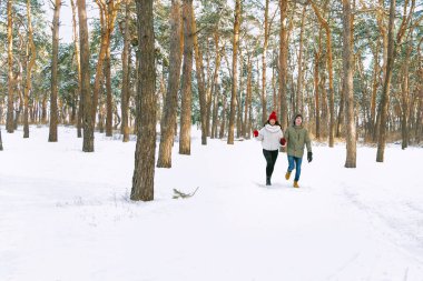 Genç çift güneşli bir günde karlı ormanda koşuyor. Park kışı.