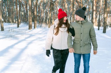Kız ve erkek kış parkında yürüyorlar ve birbirlerine bakıyorlar. Karlı ormanda genç bir çift.