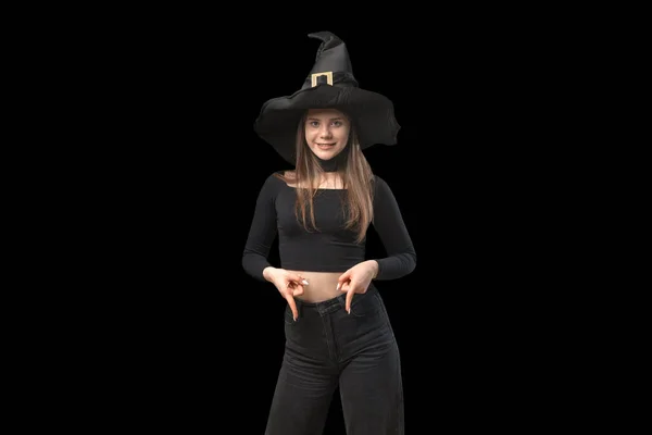 Young smiling girl in black cloth and hat fingers down. Teenager in image of witch on black background. Copy space.