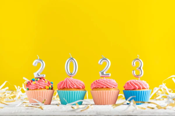 Bright Christmas theme with candles in the shape of numbers 2023 on cupcakes on yellow background. Copy space