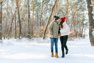 Young couple of lovers stands in the winter forest looks at each other and rub their noses holding hands. People Outdoors. Vertical frame. clipart