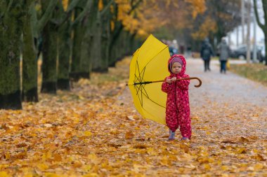 Parkta büyük sarı şemsiyeli bir sonbahar parkında küçük bir çocuk. Ayağının altındaki sarı yapraklar.