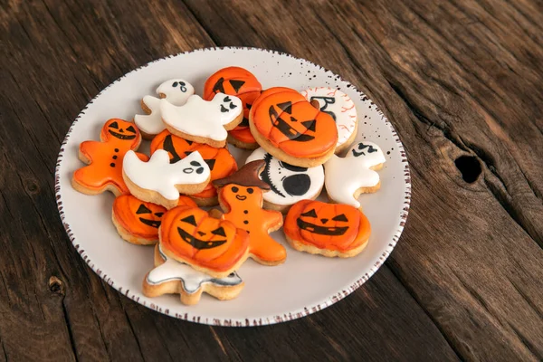 Bright orange cookies for Halloween in the shape of pumpkin ghosts in plate on a wooden table. Top view