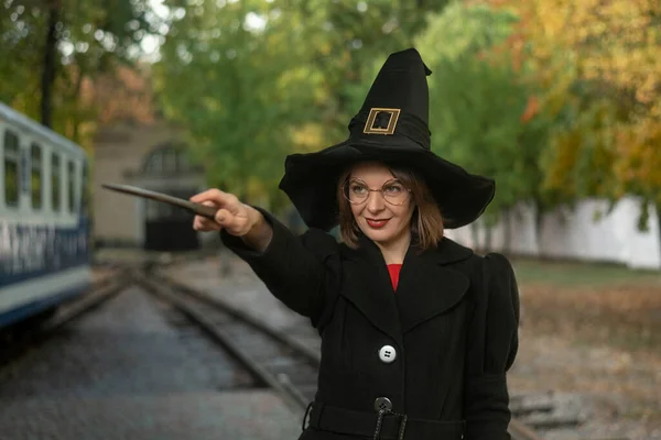 魔女の帽子 黒いコート メガネを身に着けている若い女性の肖像画 魔法の杖を手に笑顔の女の子 — ストック写真