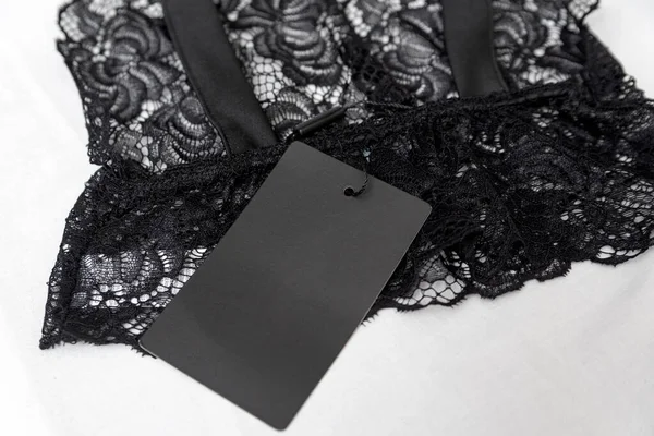 Black lace lingerie with empty black tag on white background. Transparent lace sexy bralet. Copy space.