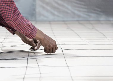 İnşaat işçisi yapısal çeliği bağlıyor, zemin beton dökümü hazırlanıyor.