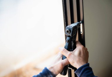 Gözlüklü, tel kapılı ve pencereli alüminyum çerçeve yapan adam inşaat alanında çalışıyor.