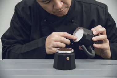 Asyalı barista moka pot kullanarak sıcak kahve yapıyor.