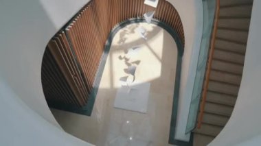 Beyaz, sarı saçlı, mavi kot ceketli ve siyah omuz çantalı genç bir kız güzel merdivenlerin yanında duruyor ve telefonuyla fotoğraf çekiyor, Şangay Starbucks, ilginç tasarım merdivenleri, modern merdivenler.
