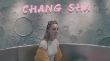 Blond hair girl in yellow coat sitting in the futuristic interior room 4K