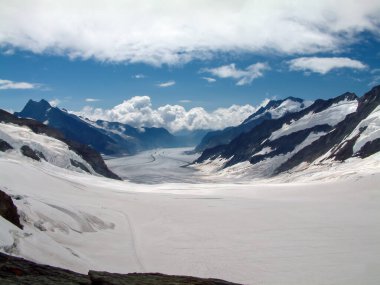 İsviçre 'deki Junfraujoch' un tepesinden bir buzul manzarası. Dağlar tarafından çerçevelenmiş buzulun ölçeğini görmek zor ama sol alttaki iki özellik buzulda yürüyen insanlar..