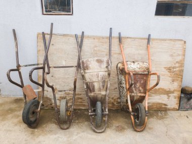 Eski ve kırık el arabaları, tahta bir tahtanın üzerinde, duvarın önüne dizilmiş.
