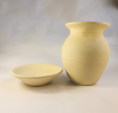 Seramik bir vazonun yakın çekimi ve temiz beyaz arka planda seramik bir tabak yan yana.