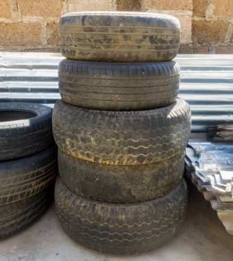 Çamurla kaplı ve dışarıda güneşte depolanmış kullanılmış lastik yığını.