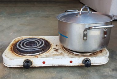 Close up on an old two plate cooking electric stove with an old used up silver pot
