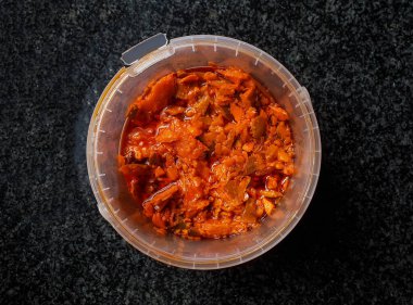 close up top view on a plastic bucket container filled with spicy mango achar which is a type of food made from unripe green mangoes pickled in oil with different types of spices.