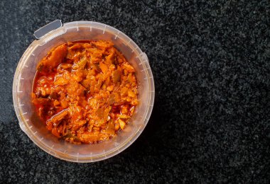 close up top view on a plastic bucket container filled with spicy mango achar which is a type of food made from unripe green mangoes pickled in oil with different types of spices.