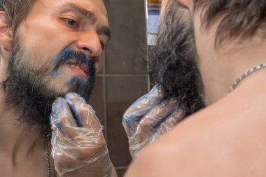 Sakallı bıyıklı bir adam sakalını maviye boyamaya çalışıyor.