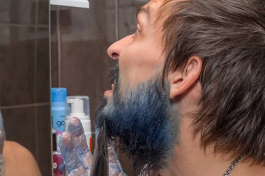 Sakallı bıyıklı bir adam sakalını maviye boyamaya çalışıyor.