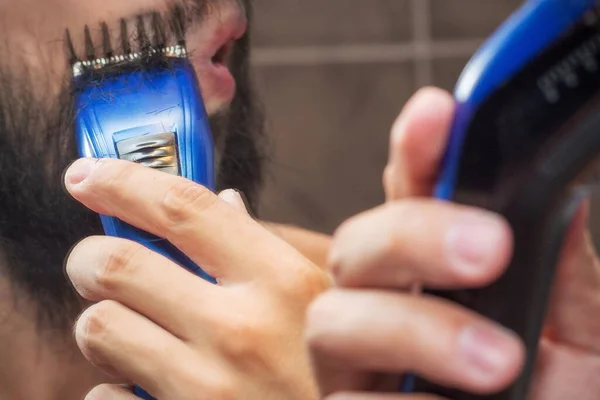 鏡の近くに電気トリマーで髭を剃る男 — ストック写真