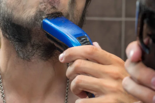 鏡の近くに電気トリマーで髭を剃る男 — ストック写真