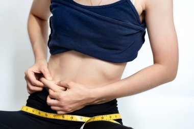 Kadın spor kıyafetleri giyiyor ve elleri beyaz arka planda göbeğini sıkıyor. Güzellik veya sağlık konsepti.