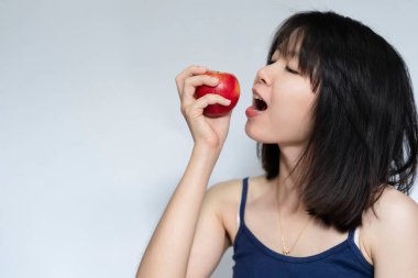 Thai 'li kadın ağzında kırmızı bir elma tutuyor ve mutlu bir şekilde yiyor. Sağlıklı gıda konsepti.